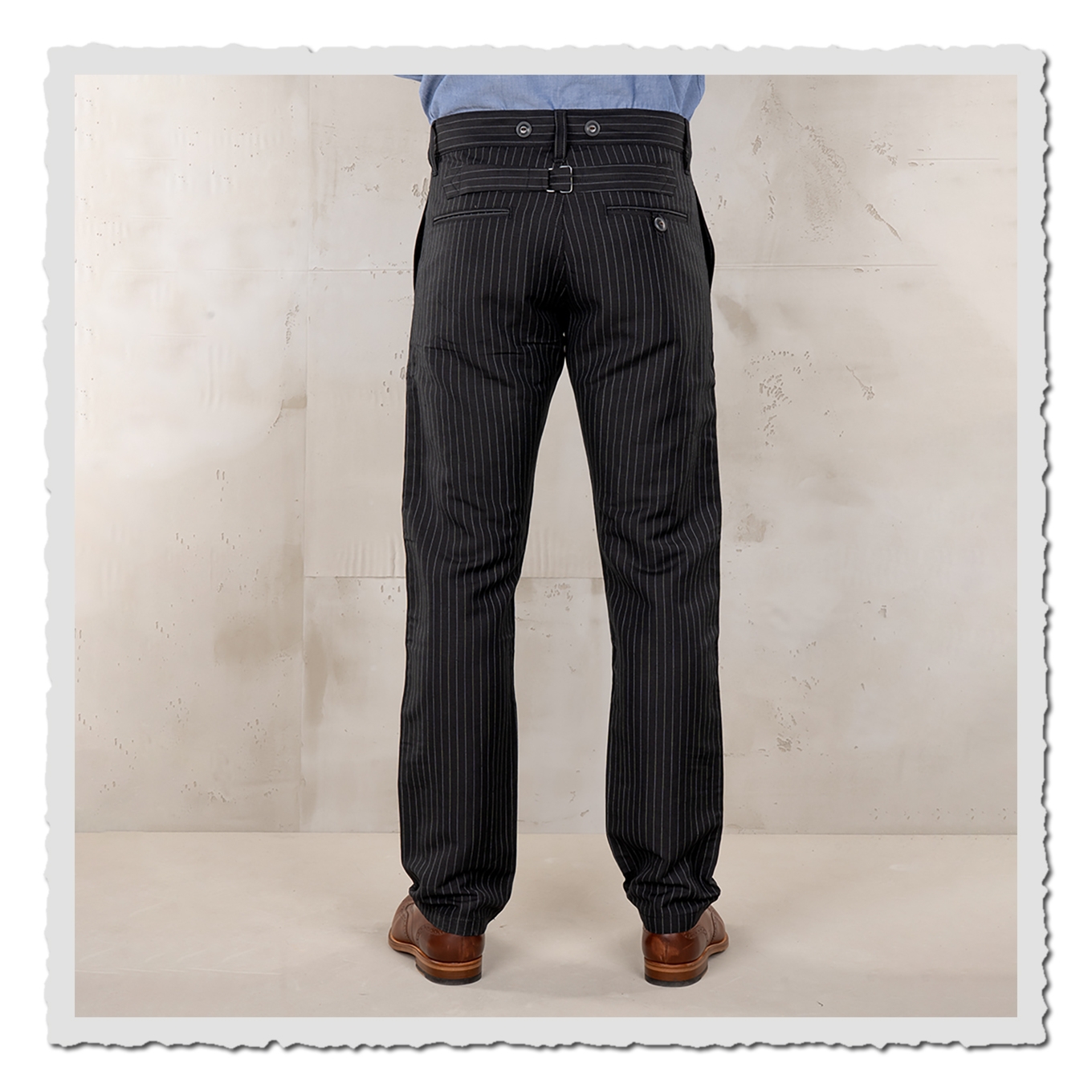 Rückansicht der schwarzen Nadelstreifen-Hose am Model, Bundbereich sichtbar, hellgrauer Studiohintergrund.